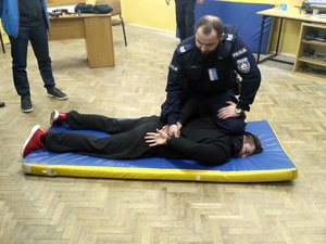 umundurowany policjant prezentuje metody kajdankowanie na leżącym na materacu pozorancie